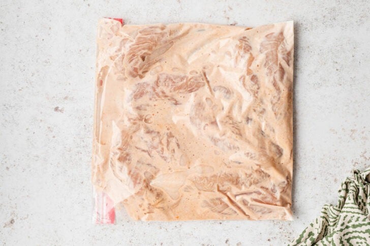 A ziptop bag filled with raw chicken tenderlons and a creamy marinade.