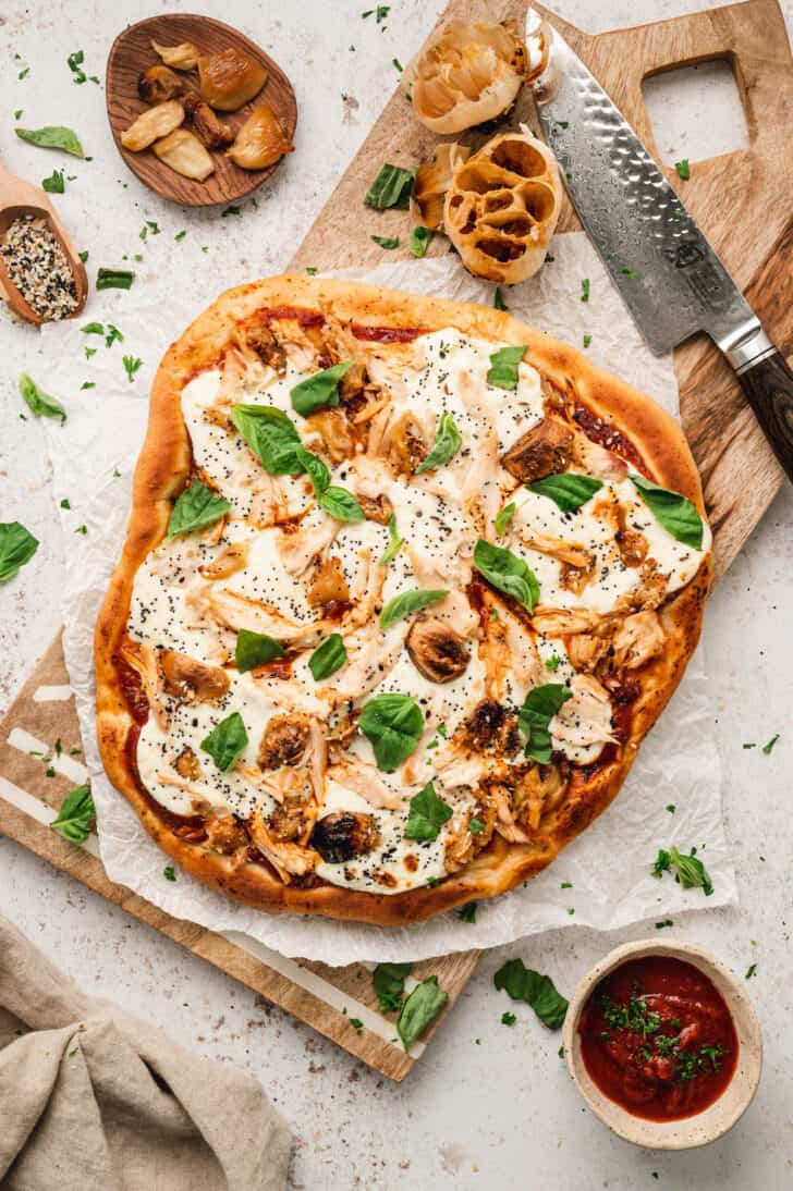 An unsliced pizza with chicken on a wooden cutting board.