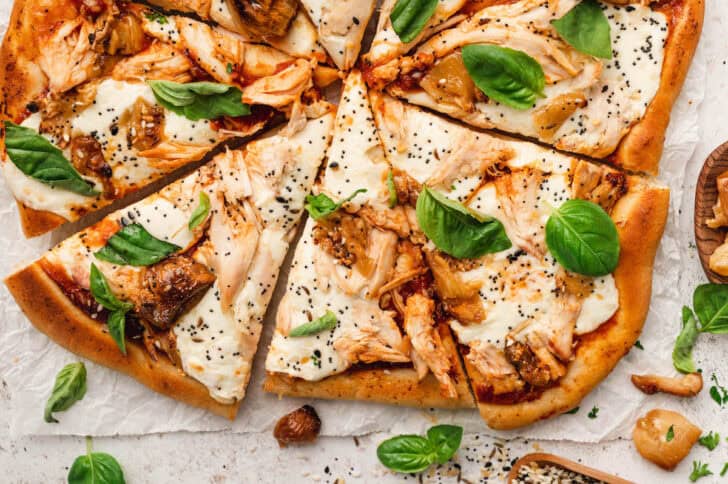 A sliced chicken pizza recipe garnished with basil.