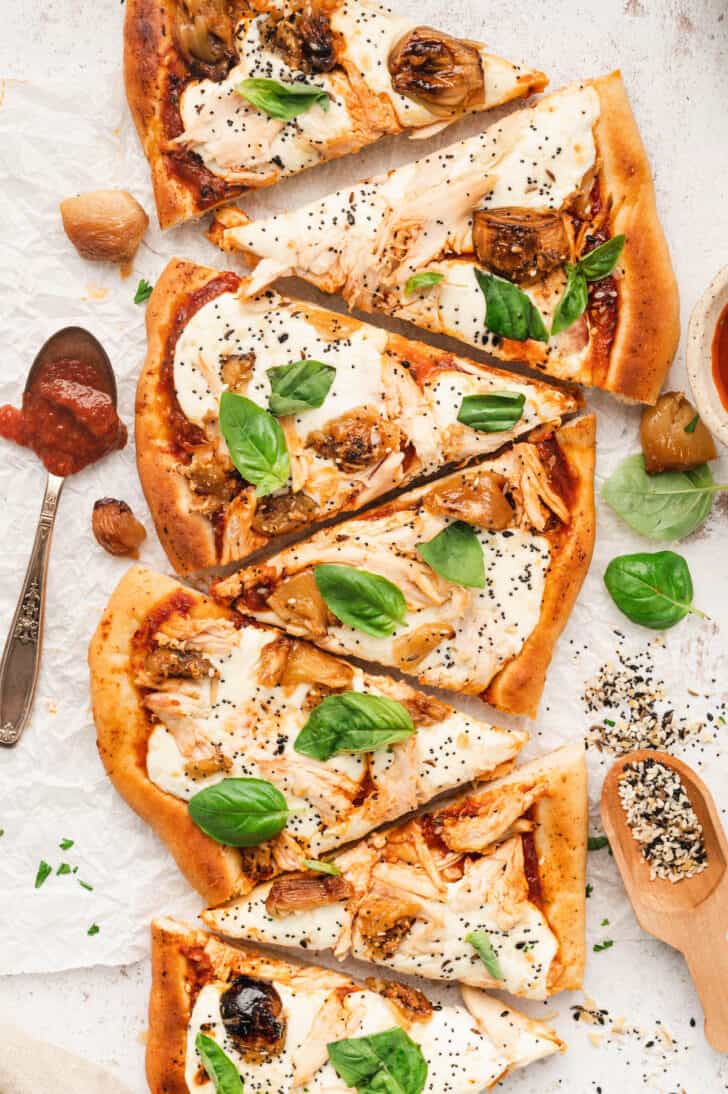 Slices of pizza with chicken and basil on a light surface.