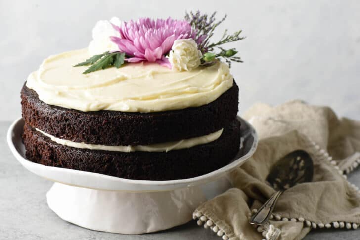 A dark, double layer cake with creamy white frosting, decorated with pink and white flowers.