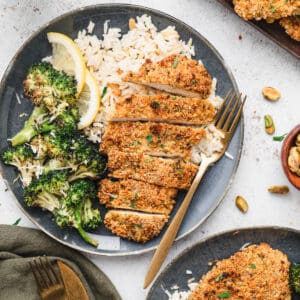 A blue plate topped with rice, roasted broccoli and sliced pistachio crusted chicken.