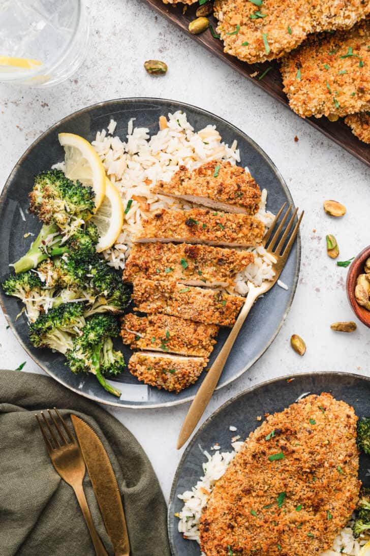 A blue plate topped with rice, roasted broccoli and sliced pistachio crusted chicken.