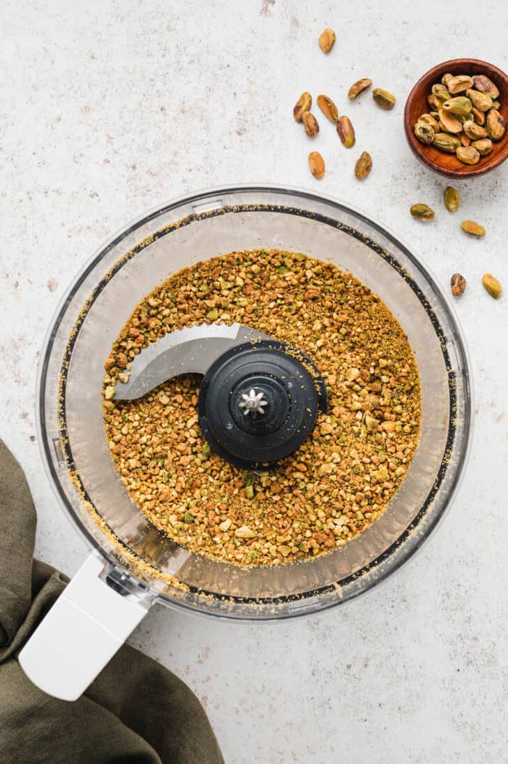 A bowl of a food processor filled with chopped pistachios.