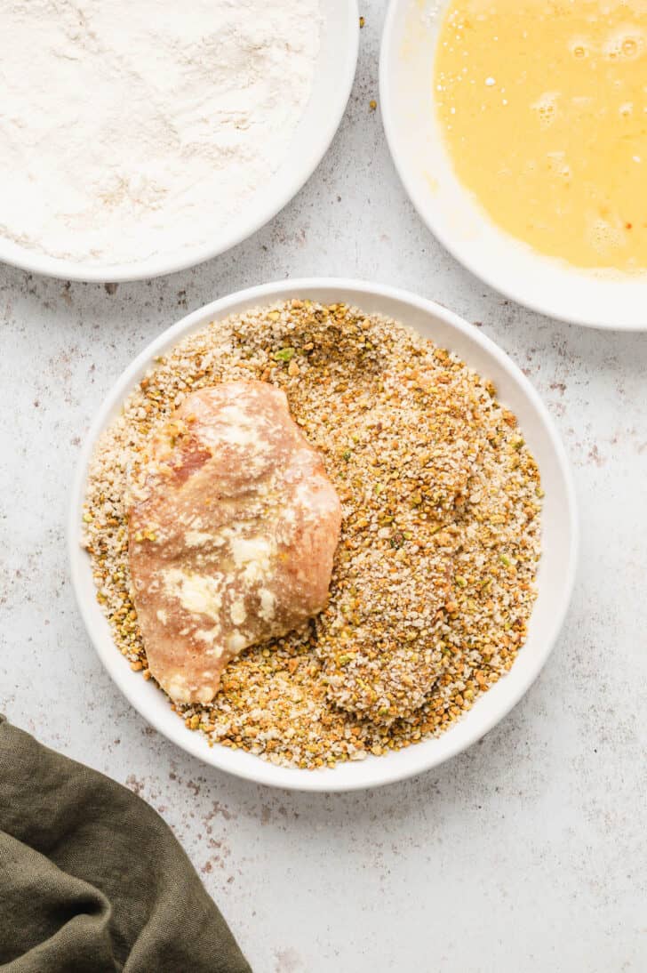 A process shot of coating chicken with pistachios in a white bowl.