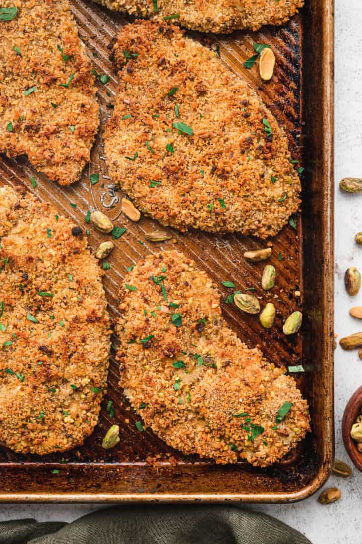 Pistachio crusted chicken breasts, baked, on a rimmed baking pan.