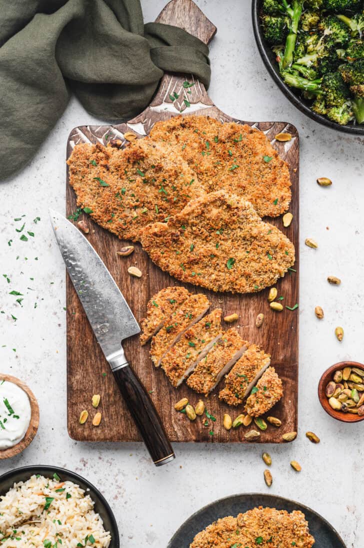 Pistachio crusted chicken breasts on a cutting board, with one piece cut into slices.