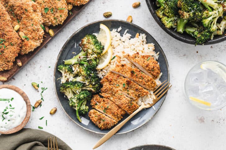 Sliced pistachio chicken on a blue plate with rice and broccoli.