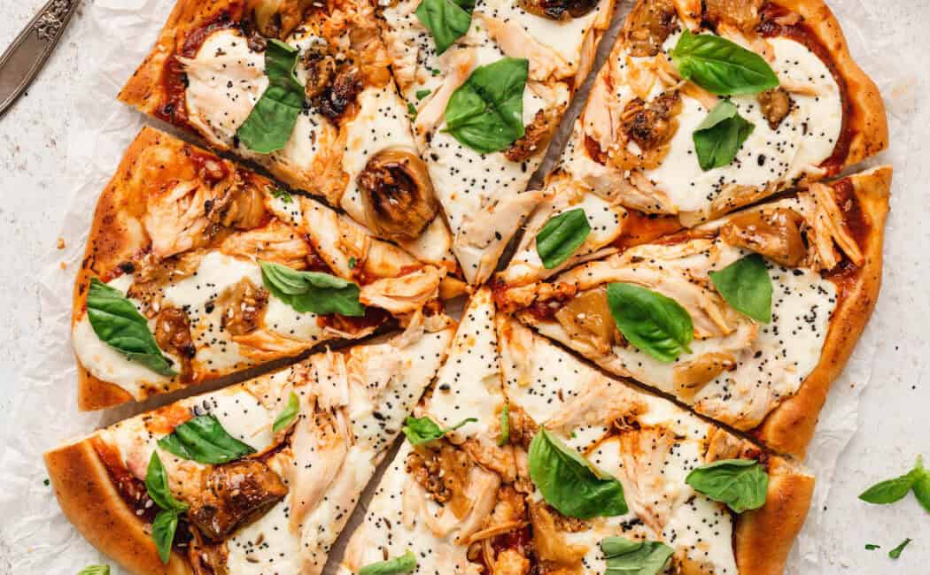 A chicken pizza topped with basil on a light surface.