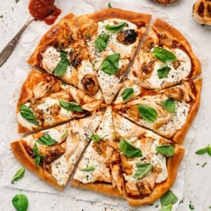 A chicken pizza topped with basil on a light surface.