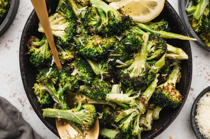 A black bowl filled with lemon Parmesan broccoli with a gold spoon digging in.