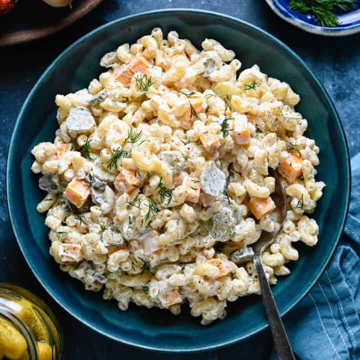 A blue bowl filled with dill pickle pasta salad made with macaroni, fresh dill and cubes of cheddar cheese.