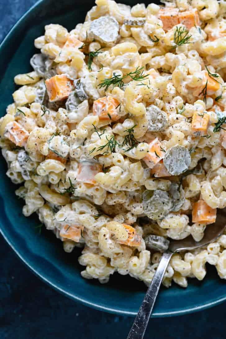 A blue bowl filled with dill pickle pasta salad made with macaroni, fresh dill and cubes of cheddar cheese.