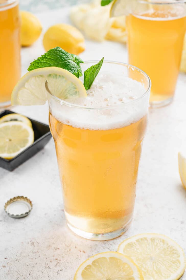 A tall glass of lemonade shandy, garnished with a lemon slice and fresh mint sprig.