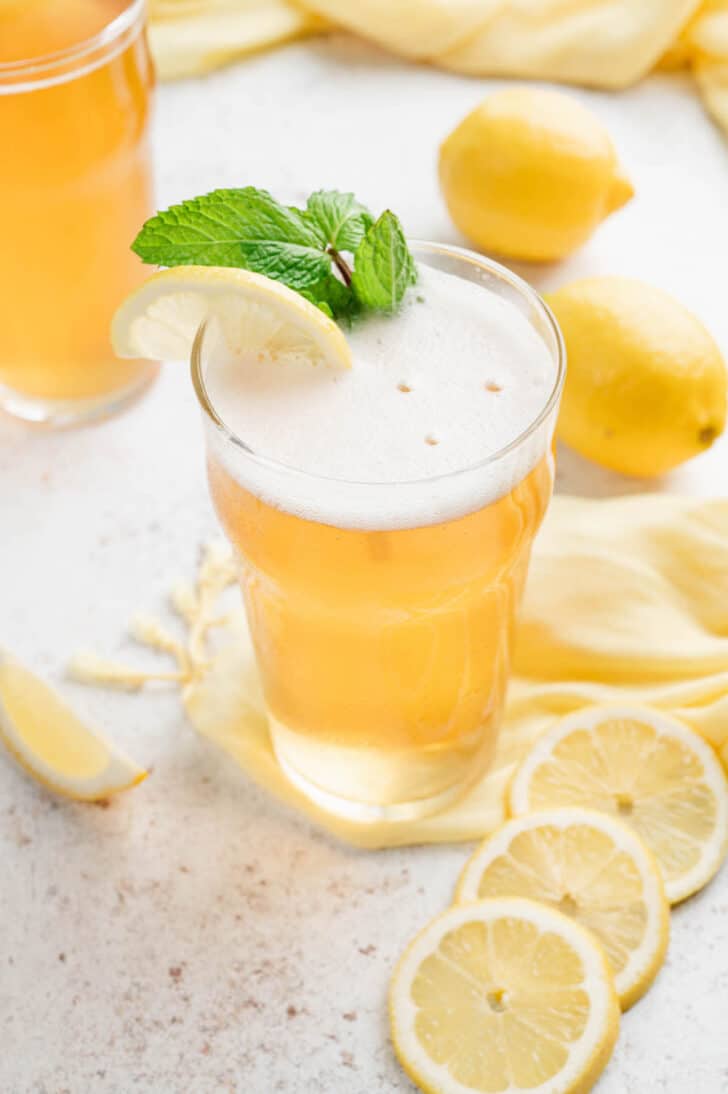 A tall glass of beer and lemonade, garnished with a citrus slice and fresh mint sprig.
