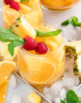 Glasses of pineapple sangria with mango over ice, garnished with raspberries and fresh mint sprigs.