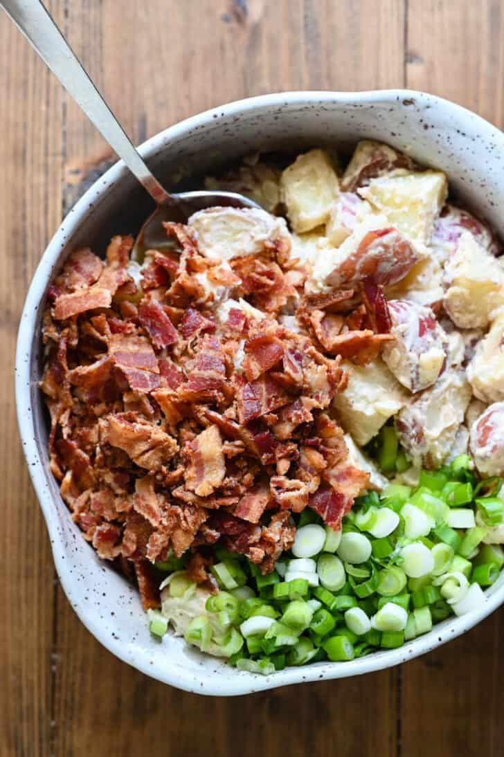A bowl of potato salad with bacon and green onions on top.