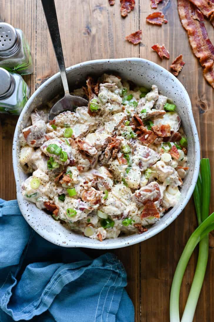 A speckled bowl filled with bacon potato salad on a wooden surface.