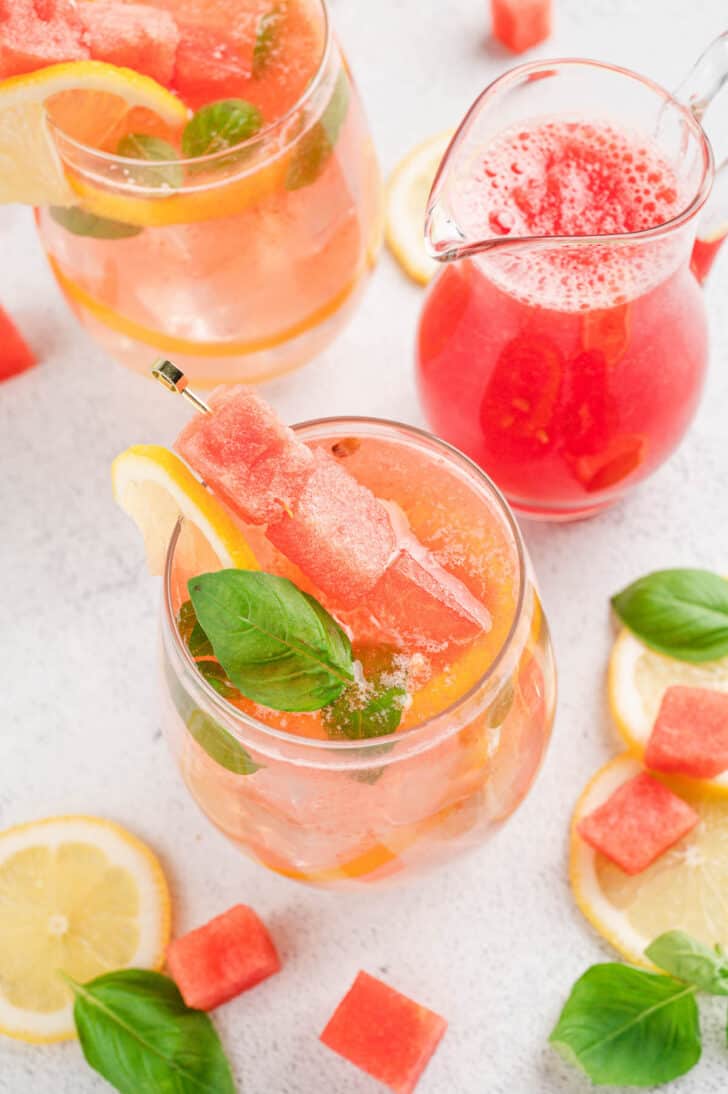A glass of watermelon basil lemonade garnished with a skewer of cubed watermelon, a lemon slice, and fresh basil leaves.