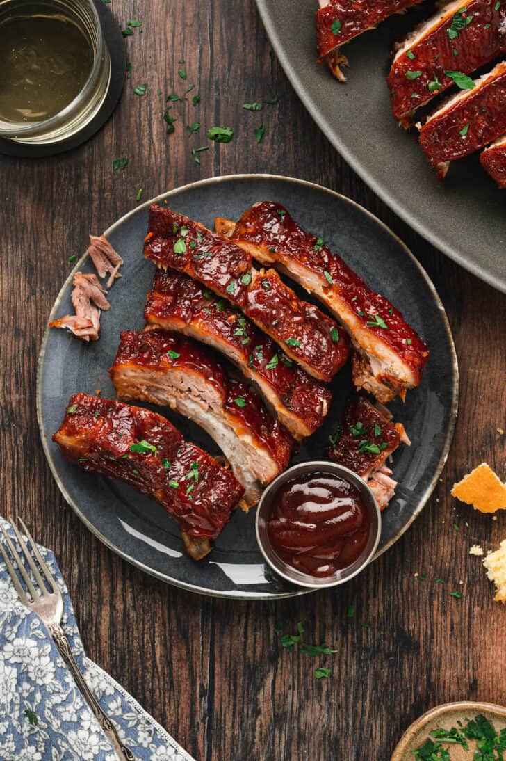 Oven baby back ribs on a blue plate with a small ramekin of barbecue sauce.