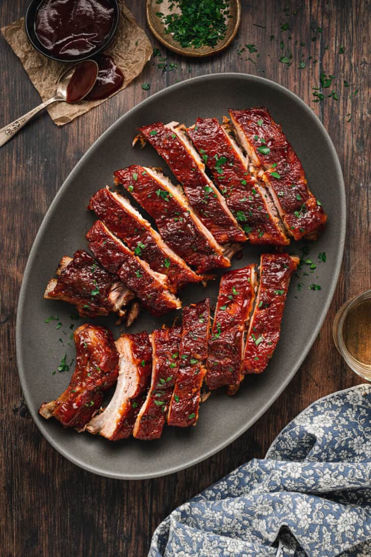 Baked baby back ribs, cut up, on gray oval platter garnished with parsley.