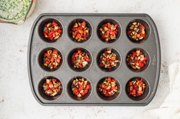 A muffin pan with the holes filled with sauteed mushrooms and red bell pepper.