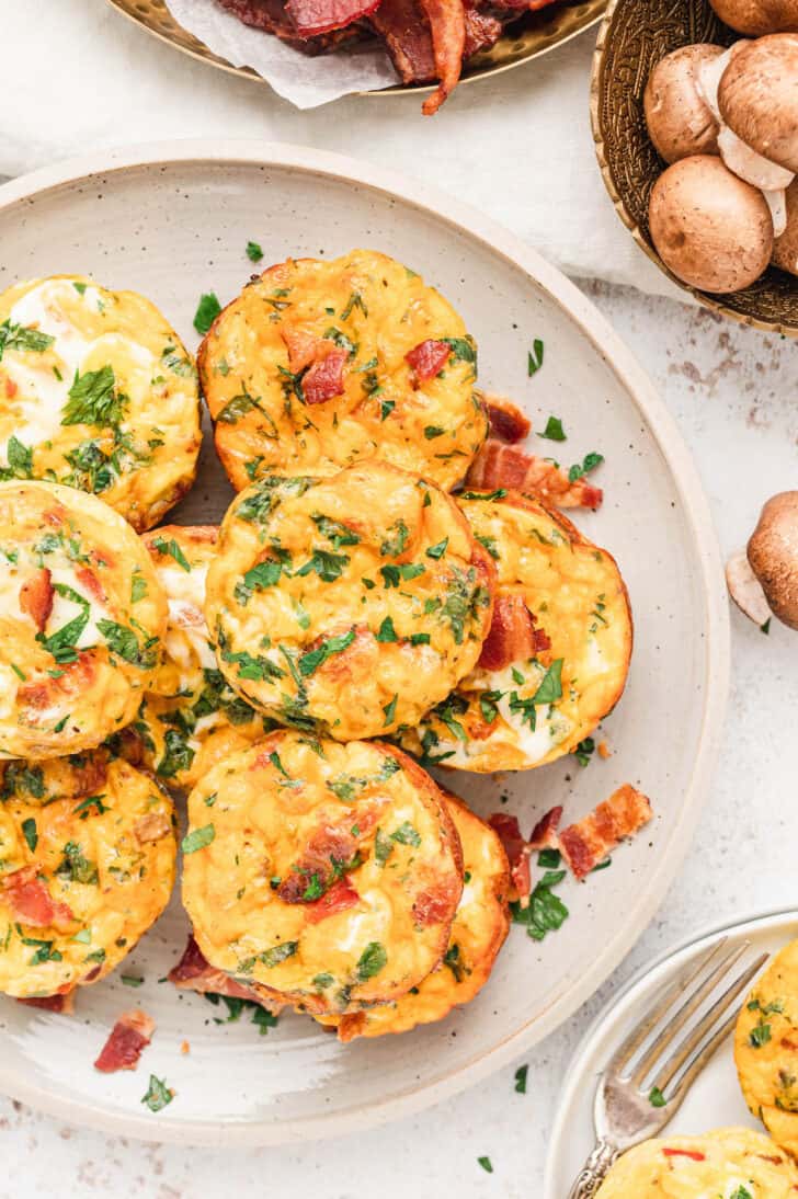 Egg muffins made with bacon, cheese and veggies piled up on a white plate.