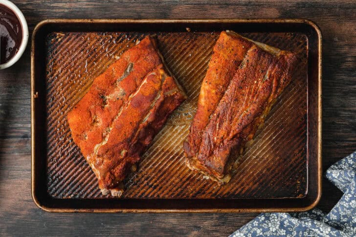 Two racks of oven baked baby back ribs on a rimmed baking pan.