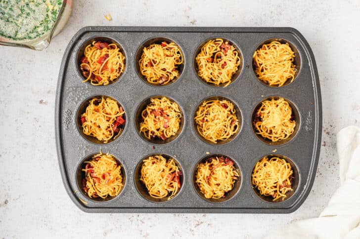 A muffin pan with the holes filled with sauteed mushrooms, red bell pepper, bacon and cheese.