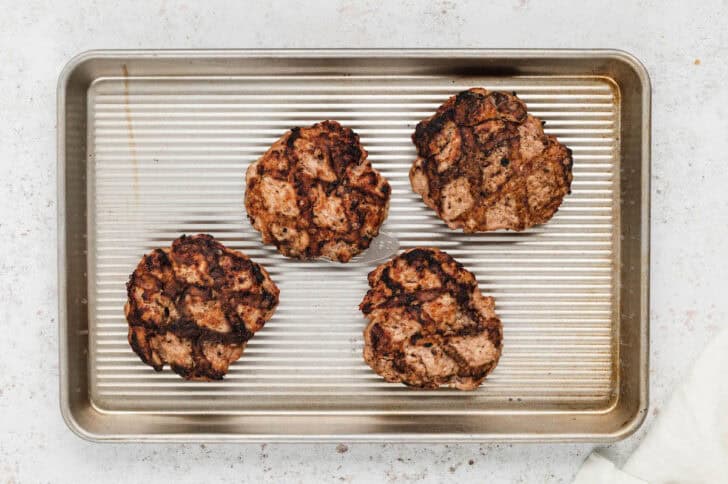 Four grilled turkey burgers on a rimmed baking pan.