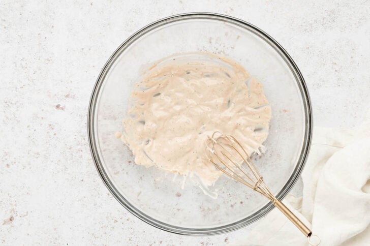 A creamy sauce being whisked together in a glass bowl.