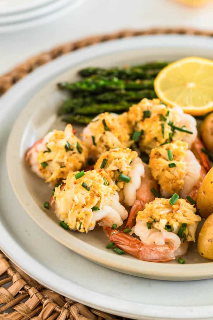 A white plate filled with stuffed shrimp with crab, asparagus, and a lemon half.