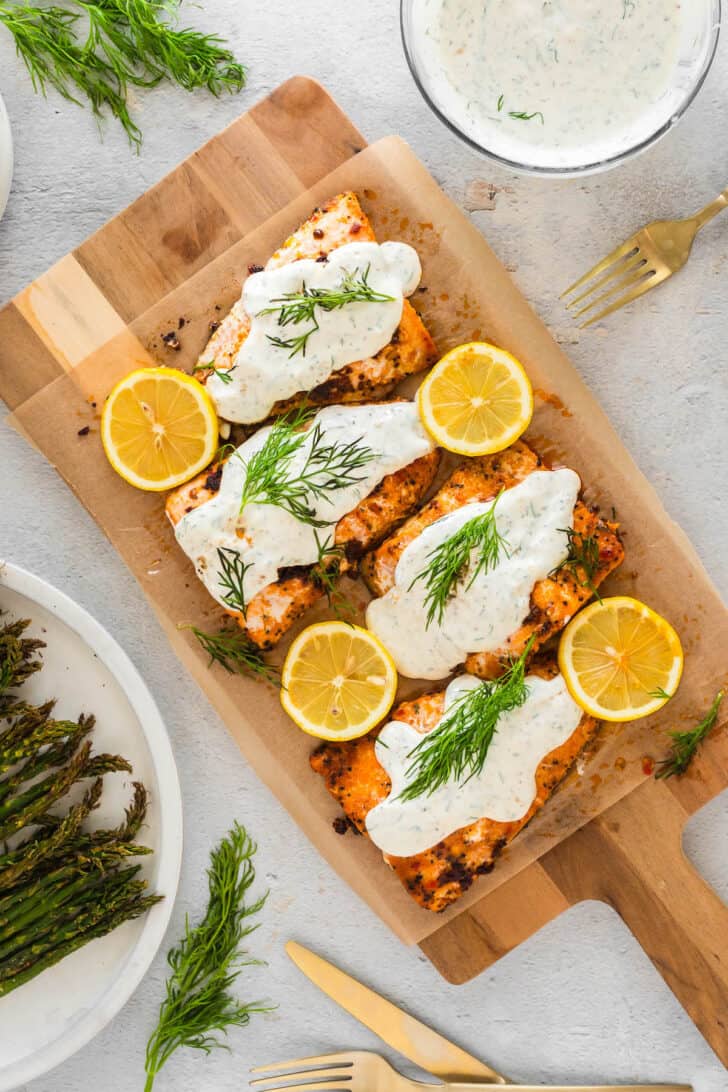Four fillets of cooked fish topped with salmon dill sauce, lemon slices, and fresh dill.