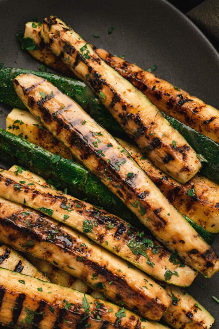 Grilled zucchini spears with a miso glaze on a dark gray platter.