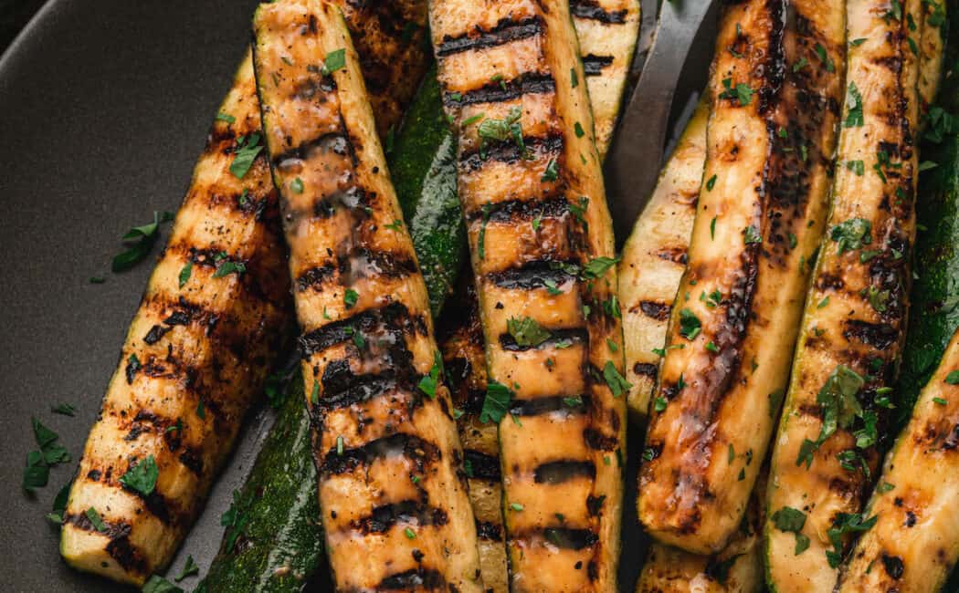 Grilled zucchini spears with a miso glaze on a dark gray oval platter.