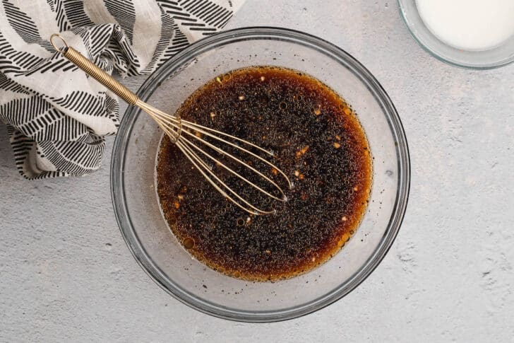 A whisk stirring together a brown sauce in a glass bowl.