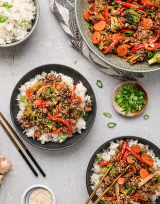 Black bowls filled with white rice topped with ground beef stir fry and veggies, garnished with green onions and sesame seeds.