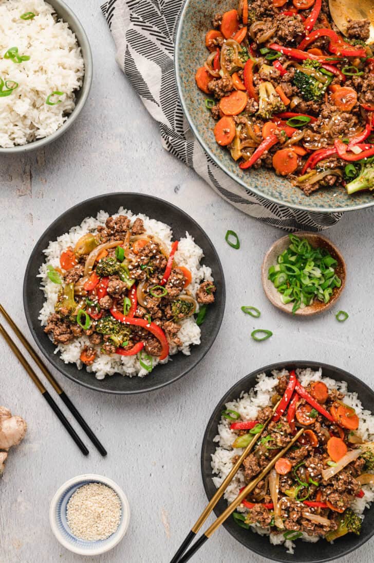 Two black bowls filled with white rice and ground beef stir fry, with chopsticks for serving.