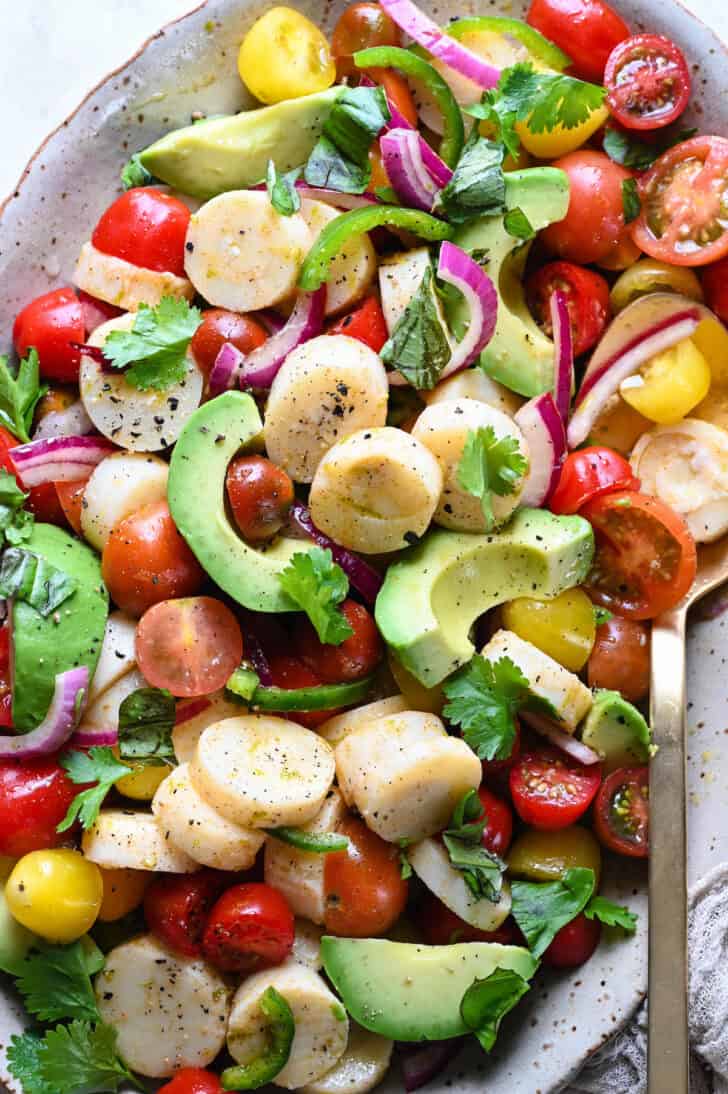 A speckled oval platter filled with hearts of palm salad made with tomatoes and avocado.