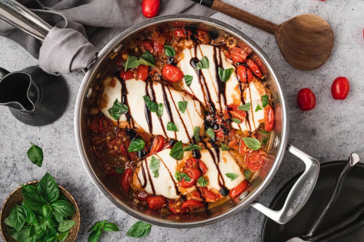 Baked caprese chicken in a skillet, finished with balsamic glaze and chopped basil.