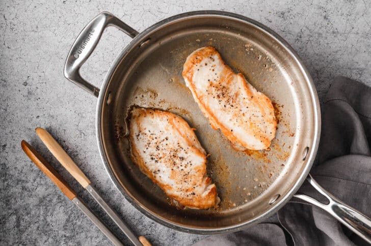 Two pieces of chicken being seared in a skillet.