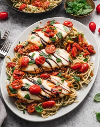 A white platter topped with baked chicken caprese over pesto spaghetti.