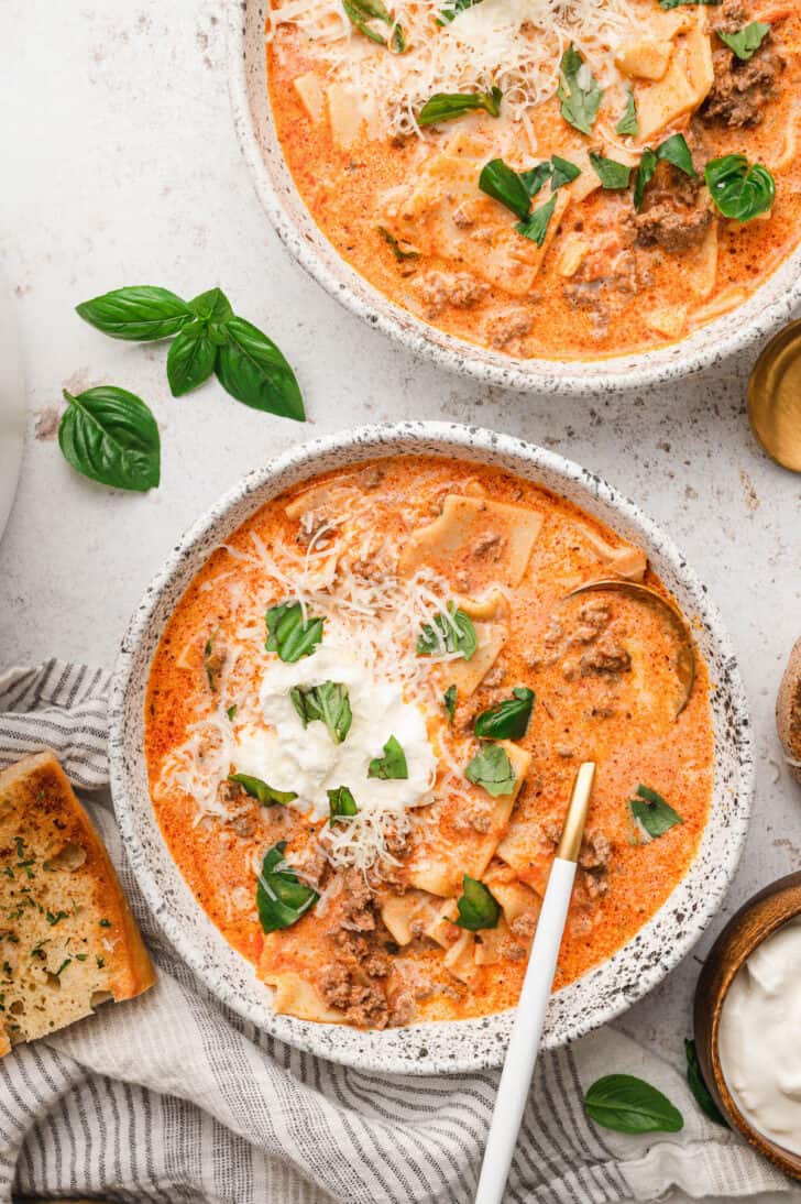 Creamy Lasagna Soup in rustic bowls, topped with ricotta, Parmesan cheese and fresh basil.