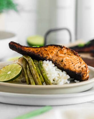 A piece of blackened salmon on top of white rice and asparagus with a lime garnish.