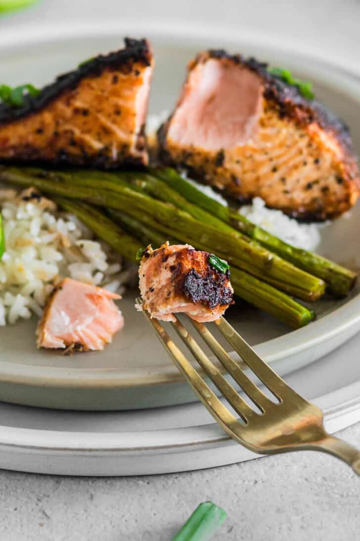 A fork holding up a bite of cast iron blackened salmon.