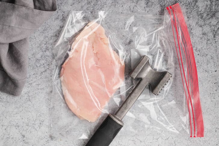 A piece of raw poultry in a plastic bag, in the process of being pounded with a meat malllet.