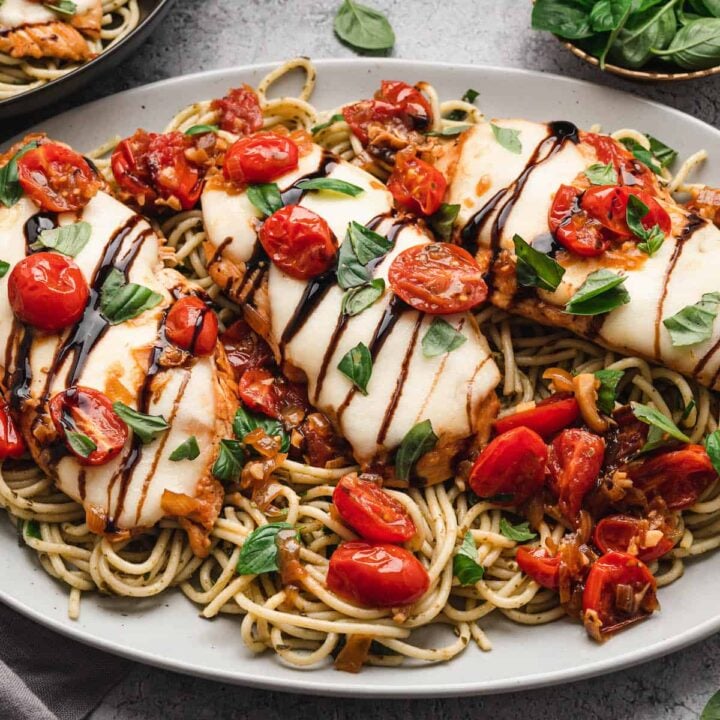 A white platter topped with baked chicken caprese over pesto spaghetti.