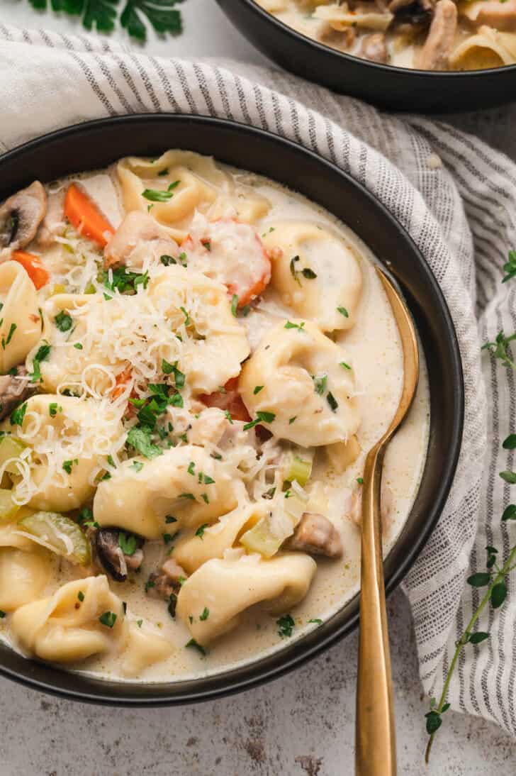 A black bowl filled with chicken and tortellini soup garnished with Parmesan cheese.