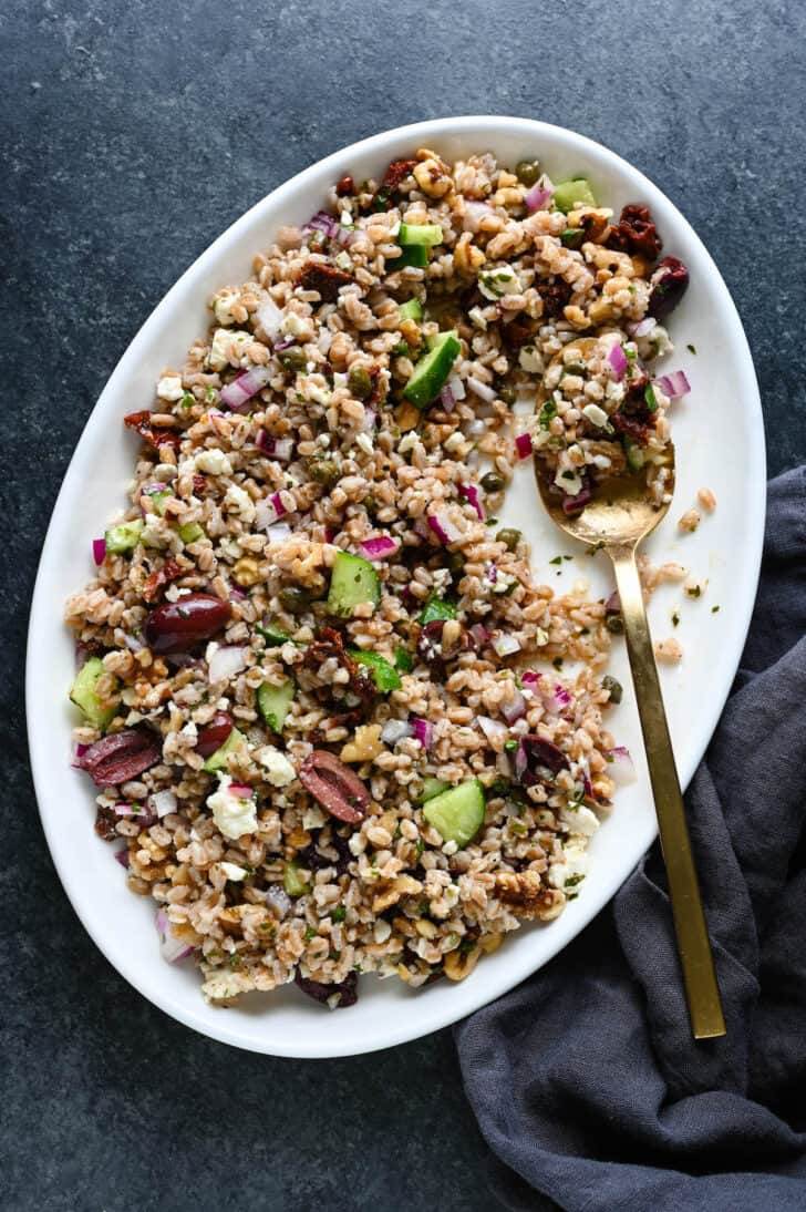 Farro salad on a white platter with a gold serving spoon digging in.
