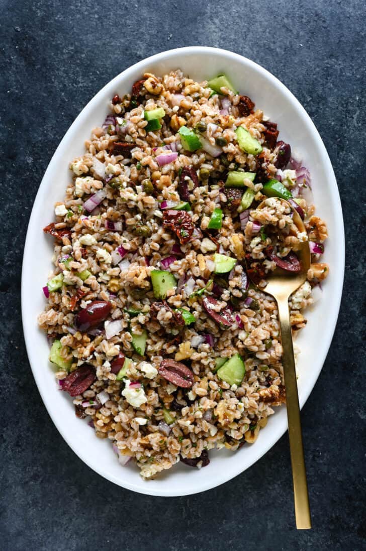 The best ever farro salad on a white platter with a gold serving spoon digging in.